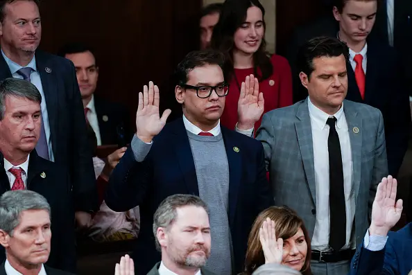 Politician George Santos is photographed raising his right hand for an oath.